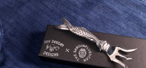 Sterling Sardine fork rests atop the black with collaborator's logos.presentation box