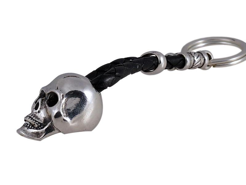 Shown is the Skull key ring, featuring a full Skull carving suspended on a braided leather cord and a split ring key holder linked to the sterling housing at the cord ends.