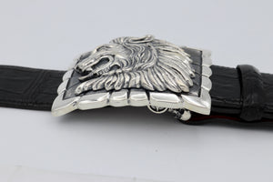 Sterling belt buckle on belt strap. Heraldic style Lion's head in profile. Sculpted in high relief atop a rectangular trophy buckle base that is textured with polished edging.  Side view.