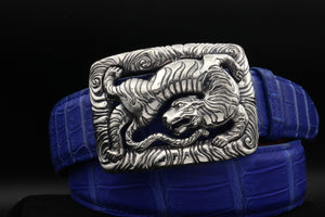 Dramatically lit front view of the Back Flipping Tiger trophy buckle , in sterling, on a coiled cobalt  blue alligator belt.