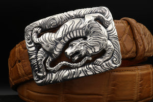 Dramatically lit front view of the Back Flipping Tiger trophy buckle , in sterling, on a coiled tan alligator belt.