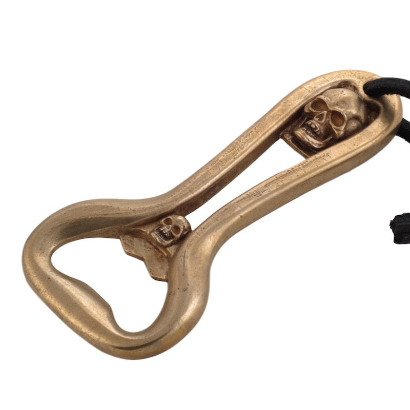 This image is of the Bronze Double Skull Bottle Opener that has 2 different sized skulls set in the handle of this opener. It hangs from a leather thong.