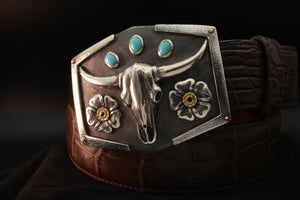 Sterling buckle with oval turquoise stones, steer skull and sterling and gold flower with rubies on a blue belt.