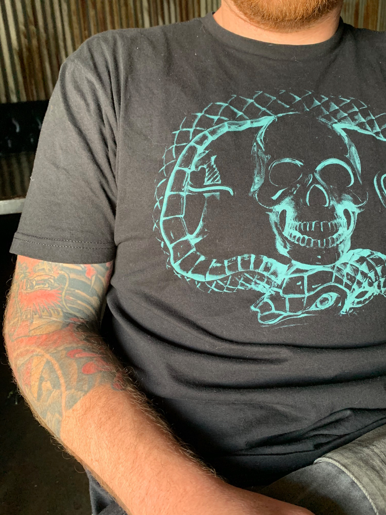 Deegan Logo T black cotton t with teal printing on front and back of Deegan buckle design