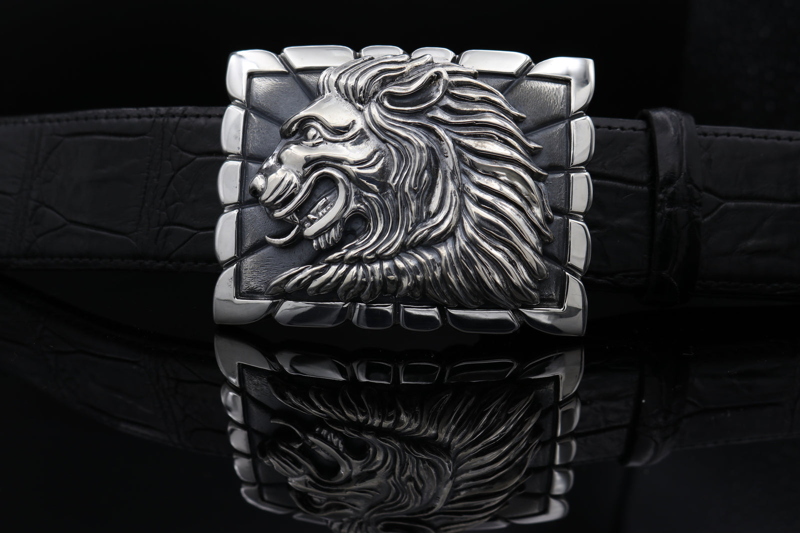 Sterling belt buckle on belt strap. Heraldic style Lion's head in profile. Sculpted in high relief atop a rectangular trophy buckle base that is textured with polished edging.  Fits 1.5" strap.